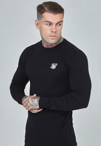 Black long-sleeve t-shirt made of smooth fabric, featuring a small white logo on the chest and fitted design accentuating the arms.