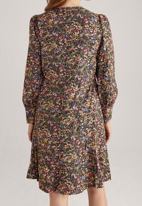 Vestido floral con mangas abullonadas largas, fondo negro, que presenta una mezcla de flores coloridas. Diseño fluido con un dobladillo ligeramente acampanado.