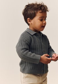 Gray knit cardigan with a textured pattern, buttoned collar, and ribbed cuffs, worn by a child, paired with beige pants.