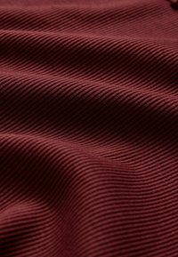 Burgundská ribbed látka s paralelnými pruhmi, ukazujúca textúru a hĺbku, jemne sa zohrýzajúca cez povrch v jemných vlnách.