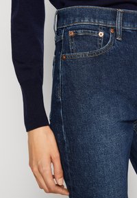 Tmavě modré džíny s vysokým pasem, měděnými nýty, podrobným prošíváním a slim fit střihem. Bavlněný materiál s jemnou strukturou.
