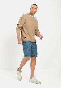 Beige, ribbet sweater med rund halsudskæring, parret med blå cargo shorts med sidelommer. Modellen bærer hvide sneakers.