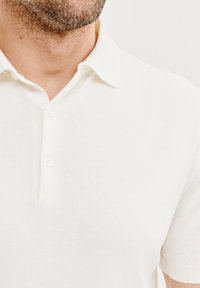 Biała, dzianinowa koszulka polo z klasycznym kołnierzykiem, trzema guzikami i krótkimi rękawami, o gładkiej, lekkiej teksturze.