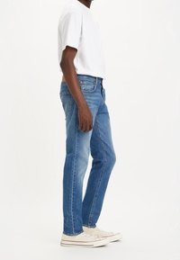 Blå denimjeans med rak passform, ljus blekning, fem fickor och sydda detaljer, tillsammans med en vit t-shirt med korta ärmar och sneakers.