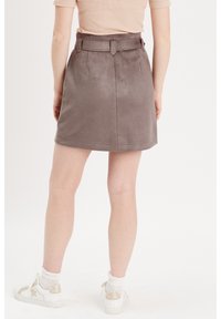Jupe en daim gris au design ajusté, avec une taille ceinturée, des accents cousus et un ourlet légèrement évasé, assortie à des baskets blanches et des chaussettes.