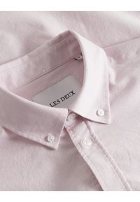 Ljusrosa, knappad skjorta med en strukturerad krage, tillverkad av textil med textur. Har vita knappar och en etikett med "LES DEUX."