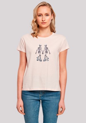 Light pink cotton t-shirt featuring a graphic of two skeletons on roller skates, short sleeves, and a relaxed fit.