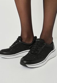 Svarta sneakers med en texturerad glittrig ovandel och släta svarta läderdetaljer. Har vit sula och svart snörning.