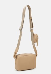Beige crossbody-väska med rektangulär form, texturerat lädermaterial, silverfärgad hårdvara och en justerbar rem med en logotyp.