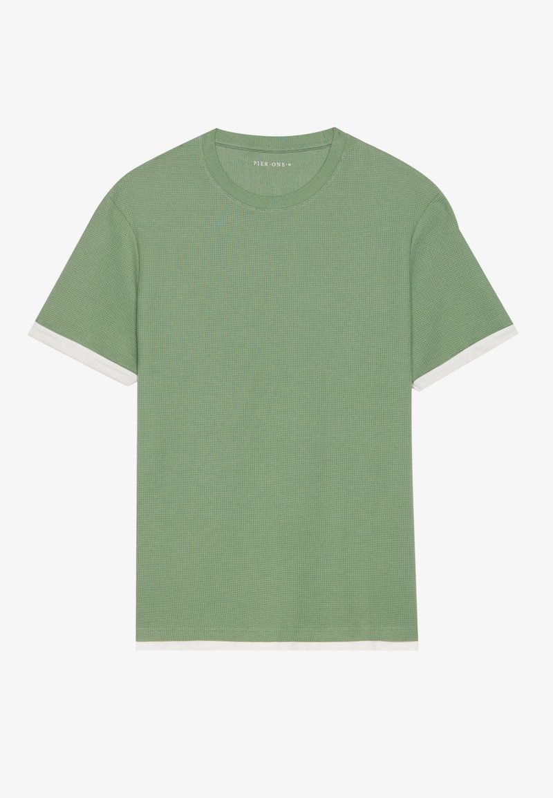 Chemise verte à manches courtes en maille gaufrée avec un col rond et une bordure blanche visible aux manches et au bas.