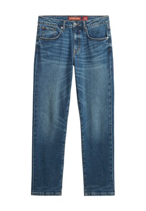 Jeans de mezclilla azul con corte recto, desgastados en los muslos, cinco bolsillos y costuras en contraste. La etiqueta dice "Superioridad de la Mezclilla".