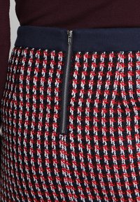 Neulottu hame, jossa on punainen, valkoinen ja laivastonsininen ruutukuvio, laivastonsininen joustava vyötärönauha ja sivulla oleva vetoketjutekstiili.