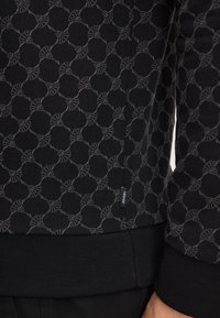 Czarna bluza z geometrycznym szarym wzorem, ściągacze u rękawów i mała metka "JOOP!" z boku. Miękka, teksturowana tkanina.