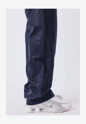 Dunkelblaue Denimjeans mit einer entspannten Passform und glatter Textur. Kombiniert mit weißen Sportschuhen mit silbernen Akzenten.