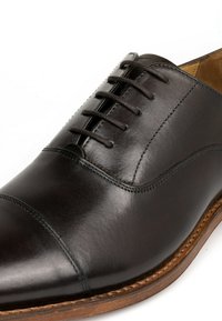 Scarpa nera in pelle con lacci, dalla texture liscia, punta arrotondata e un dettaglio di cucitura a contrasto lungo il bordo della suola.