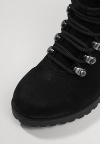 Zwarte enkellaars met een gestructureerd oppervlak, voorzien van zwarte veters door metalen veterogen en een robuuste rubberen zool.