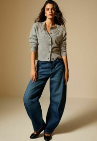 Cardigan grigio con decorazioni sulle spalle, abbinato a jeans scuri a vita alta e ballerine nere.