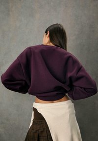 Fialový skrátený sweatshirt s prehnanými rukávmi, textúrovaná tkanina, rebrovaný lem, v kombinácii s vrstvenou sukňou s rebrovanou bielou časťou.