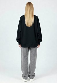 Sweat-shirt noir oversize et pantalon large gris, avec poignets côtelés et texture douce, assortis à des baskets blanches.