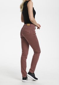 Vaqueros skinny-fit de color rosa con una textura suave, cinco bolsillos y una etiqueta de marca de cuero en la parte posterior de la cintura. Combinados con zapatos negros.
