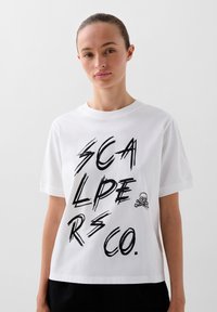 Hvid bomulds T-shirt med stort sort grafisk tekst "SCALPERS CO." og en lille dødningehoved- og korsbenaccent. Normal pasform, korte ærmer.