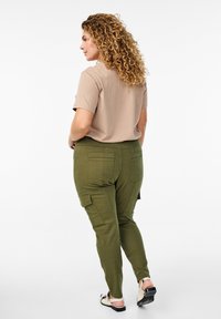 Bēšas krāsas īsām piedurknēm T-krekls, kas apvienots ar olīvu zaļām biksēm ar sānu kabatām, šauru piegriezumu un gludu auduma faktūru.