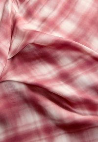 Un tissu à carreaux rose et blanc avec une texture douce. Le design se compose de carrés et de lignes flous, créant une apparence légère.