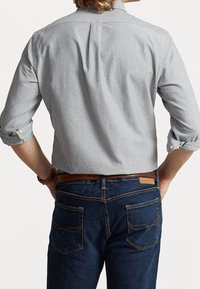 Camicia grigia chiaro con maniche arrotolate, abbinata a jeans in denim blu scuro con cuciture a contrasto e due tasche posteriori.