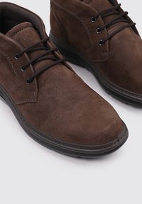 Zapatos de hombre casuales de cuero marrón con cordones, suelas negras y detalles de costura, sobre un fondo blanco.
