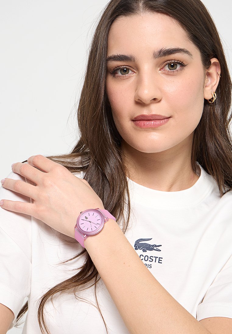 Orologio da polso in silicone rosa con quadrante rotondo, indicatori dell'ora semplici e una texture liscia, indossato su un polso contro una maglietta bianca.