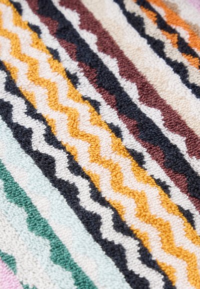 Gros plan d’un tissu texturé avec des rayures ondulées diagonales en jaune, noir, blanc, marron, vert et bleu clair.