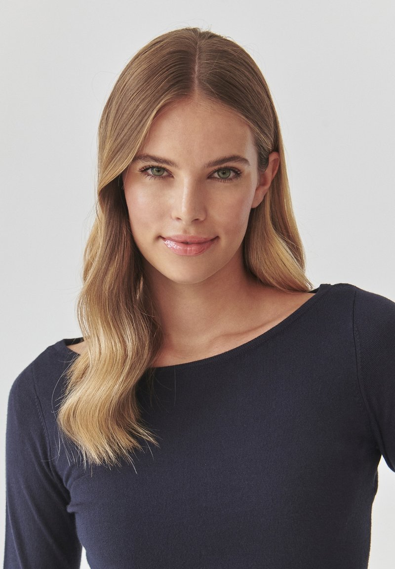 Granatowa bluzka z długim rękawem o okrągłym dekolcie, wykonana z prążkowanej tkaniny. Gładka faktura, dopasowany krój, minimalistyczny styl.