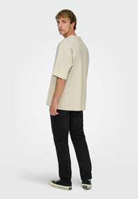 Beige oversized t-shirt med korte ærmer og rund halsudskæring, kombineret med sorte jeans og sorte sneakers med hvide såler.