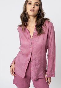 Camicetta di lino rosa chiaro con bottoni sul davanti, maniche lunghe e una vestibilità rilassata. Tessuto testurizzato con spacchi laterali e bottoni argentati.