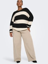 Mustvalge triibuline kootud kampsun lõdva istuvusega, millele on lisatud beežid laia säärisega sametpüksid ja mustad teravate varbavahelistega kingad.