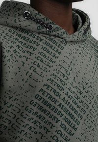 Felpa verde in misto cotone con superficie texturizzata, dotata di testo stampato scuro e coulisse regolabile nel cappuccio.