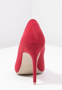 Rode hoge hak schoen, gemaakt van suède materiaal, met een puntige neus, slanke stilettohak en een gladde beige zool.