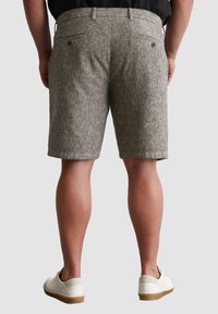 Graue gestreifte Shorts mit lockerer Passform, flachem Bund, zwei Gesäßtaschen und Seitennähten. Getragen mit weißen Freizeitschuhen.