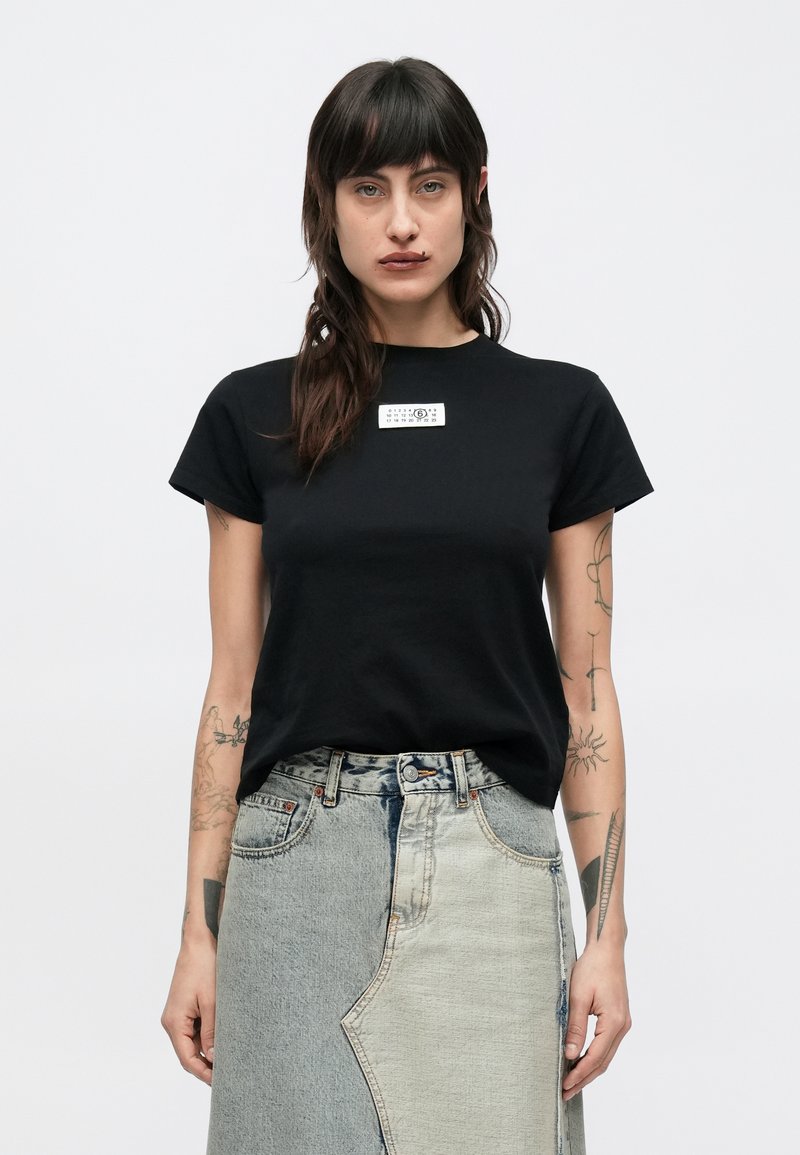 Zwart katoenen T-shirt met korte mouwen, met een klein rechthoekig label met tekst op de borst. Gecombineerd met een lichtblauwe jeansrok met patchwork.