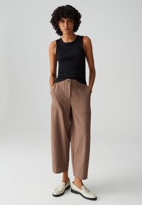 Zwarte mouwloze top, bruine wijde broek met voorzakken en een knoopdetail. Complementeert met off-white loafers met zwarte zolen.