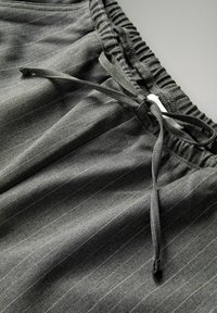Grå stribede shorts lavet af stof med en elastisk talje og en snorelukning. Har subtile lodrette linjer og en blød tekstur.