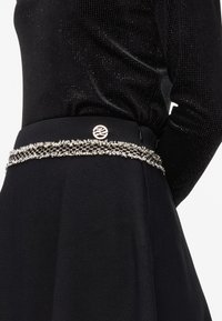 Black skirt with a textured surface, accented by a metallic trim and logo at the waist. The design features a flared shape.