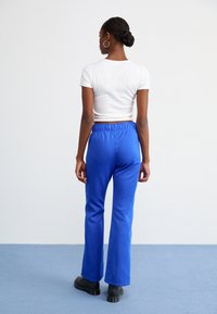 Blue flared pants with an elastic waistband, made from smooth fabric. Paired with a fitted white short-sleeve top and black footwear.