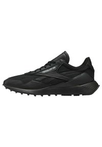 Scarpa atletica nera con una combinazione di materiali in mesh e pelle, suola testurizzata e dettagli a contrasto con il marchio sul lato.