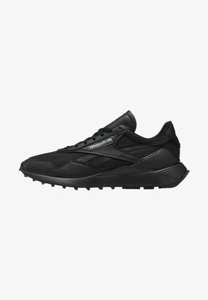 Black athletic shoe featuring a mix of mesh and leather materials, a textured sole, and contrasting accents with branding on the side.
