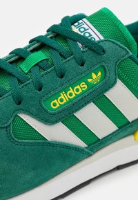 Zapatillas de deporte de ante verde y malla con franjas blancas, logotipo amarillo y cordones texturizados. Cuenta con un collar acolchado y suela de goma.