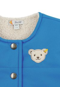 Giacca blu per bambini con un morbido interno in pile, con applicazione di orsetto e chiusura a scatto in metallo. Etichetta con la scritta "Steiff," taglia 62.