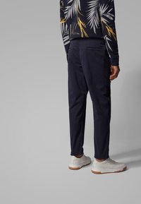 Navy blue trousers with a straight fit, lightweight fabric, elastic waistband, and subtle back pocket detail, paired with white sneakers.