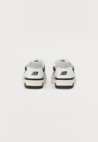 Tênis brancos com detalhes em preto e cinza. Apresenta um cabedal sintético suave, calcanhar acolchoado e sola de borracha texturizada com padrão de aderência visível.