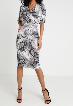 Černobílé šaty se vzorem hadí kůže, zavinovacího střihu, s krátkými rukávy, přiléhavým střihem a délkou pod kolena. Černé sandály na podpatku s pásky.